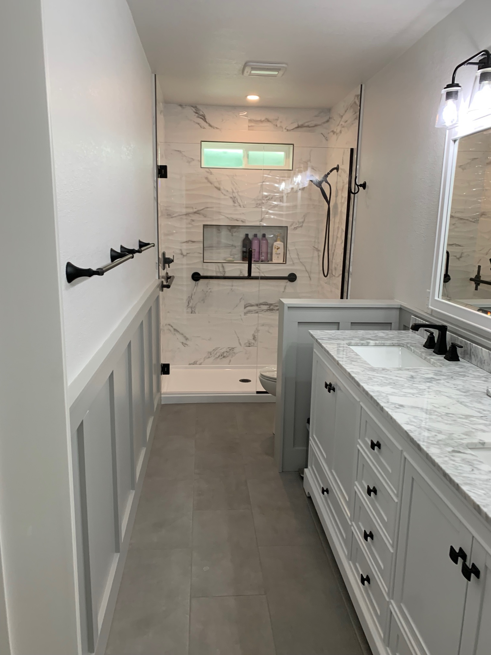 Hollister bathroom with marble vanity, wainscot paneling, matte black hardware